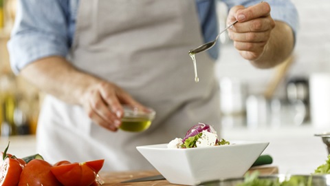 homem a temperar salada com uma colher de azeite